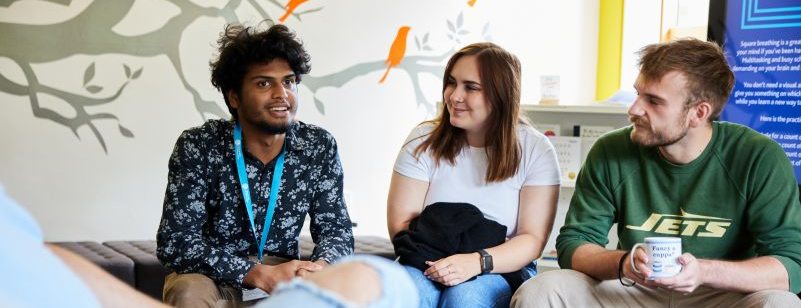 Three students having a friendly conversation in a bright support lounge